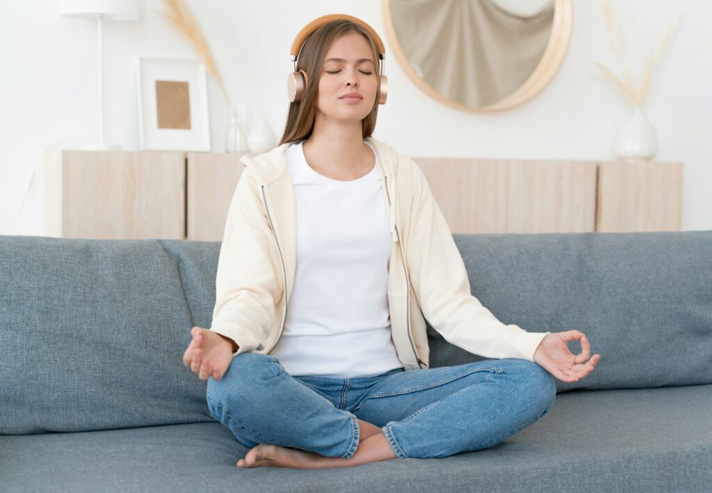 Calm young woman sitting on couch, practicing meditation yoga with mudra hands