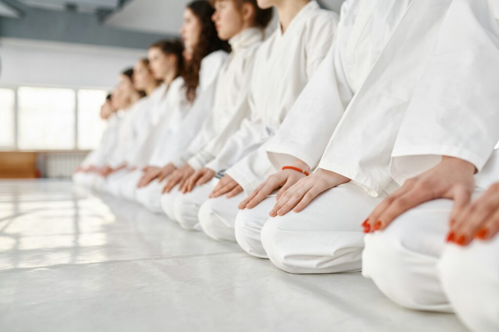 Young woman team in white martial arts uniform sitting on floor in gym
